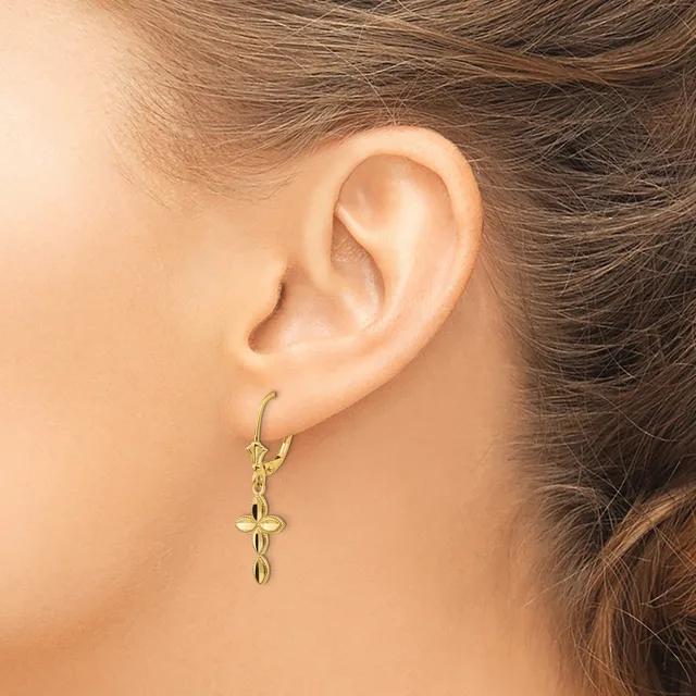 A person wearing gold-toned cross-shaped dangle earrings with a small hallmark, shown from the side against their ear.