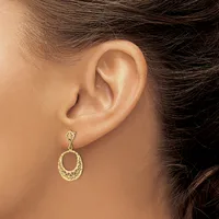 A person wearing a gold filigree oval dangle earring with a smaller matching stud earring on their earlobe.