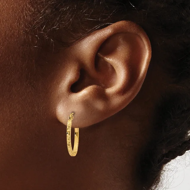A close-up side view of a person's ear wearing a textured gold hoop earring with a small hallmark stamp visible on the post.
