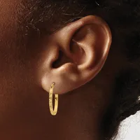 A close-up side view of a person's ear wearing a textured gold hoop earring with a small hallmark stamp visible on the post.