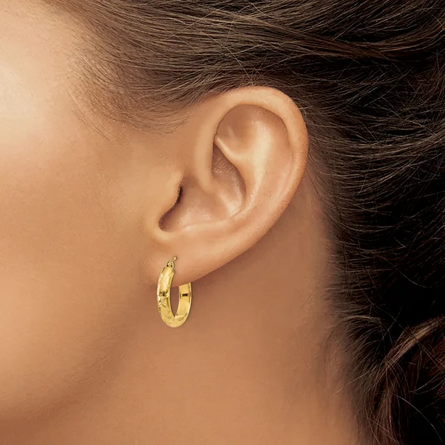 A person wearing a pair of gold hoop earrings with a textured surface, shown from the side profile of their face and ear.