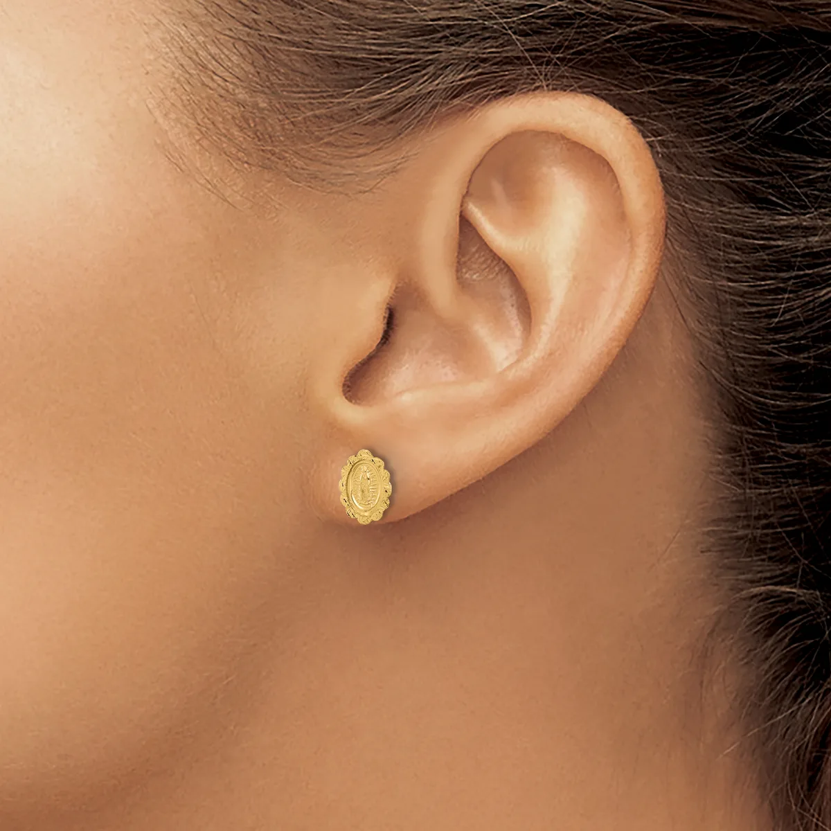 A person wearing a small oval gold stud earring with a textured surface in their earlobe.