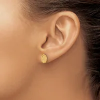 A person wearing a small oval gold stud earring with a textured surface in their earlobe.