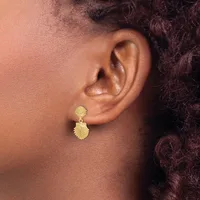 A person wearing gold-textured drop earrings with a scalloped shell-like design on both the upper and lower portions of each earring.