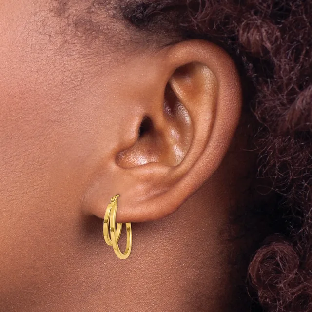 A person wearing a pair of gold hoop earrings with a polished finish, shown from the side profile.