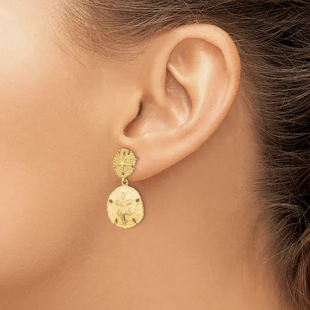 A woman wearing gold drop earrings with textured round studs and larger teardrop-shaped pendants featuring a stamped pattern.