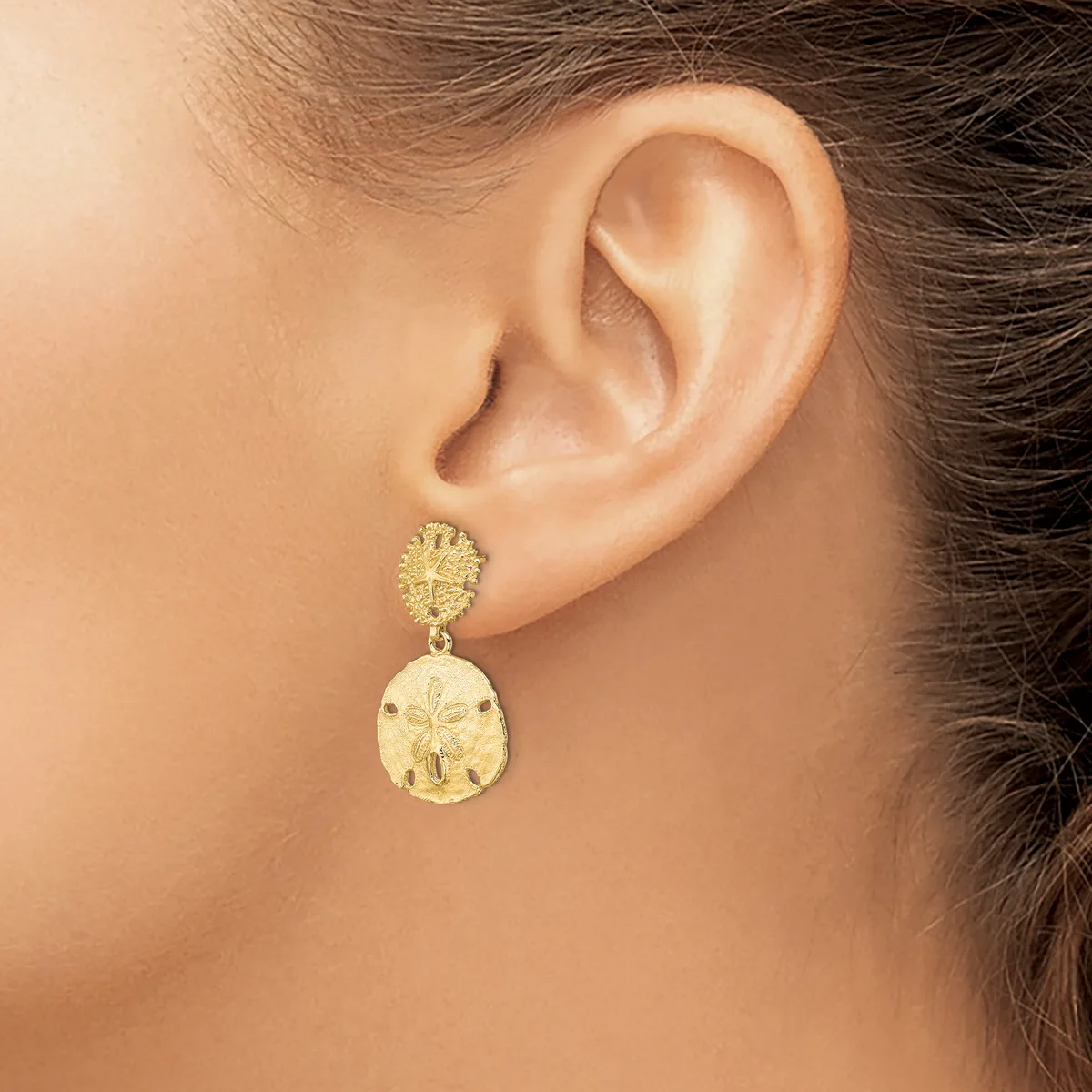 A woman wearing gold drop earrings with textured round studs and larger teardrop-shaped pendants featuring a stamped pattern.