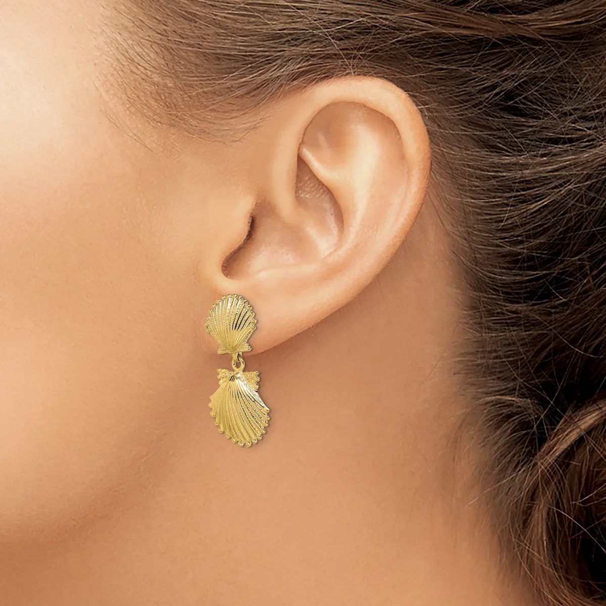 A person wearing gold shell-shaped drop earrings with textured surfaces, shown from the side profile of their ear and neck.