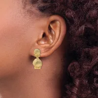 Gold shell-shaped drop earrings worn on a person's ear, with textured finish and small post fittings.