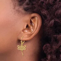 A gold dragonfly charm earring hangs from a gold hoop on a person's ear, with dark curly hair visible in the background.