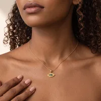 A woman with curly brown hair wearing a gold chain necklace with a small evil eye pendant featuring a green stone.