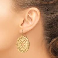 A gold filigree teardrop earring with ornate scrollwork hangs from a wire hook on a model's ear.