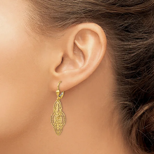 A woman wearing a gold-toned filigree drop earring with an elongated leaf or marquise shape hanging from a hook clasp.