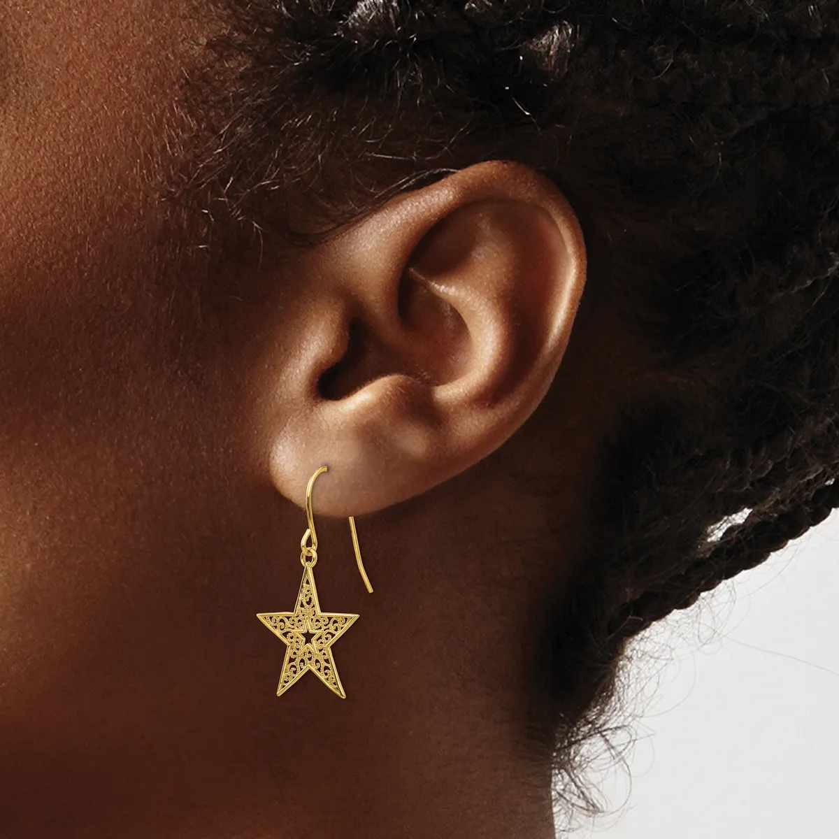 A person wearing gold star-shaped drop earrings with openwork filigree detail, shown in profile against a neutral background.