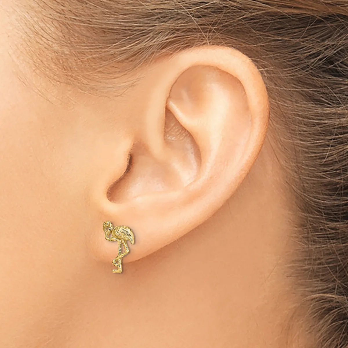 A gold-toned flamingo-shaped stud earring worn on a person's earlobe, shown from the side view.