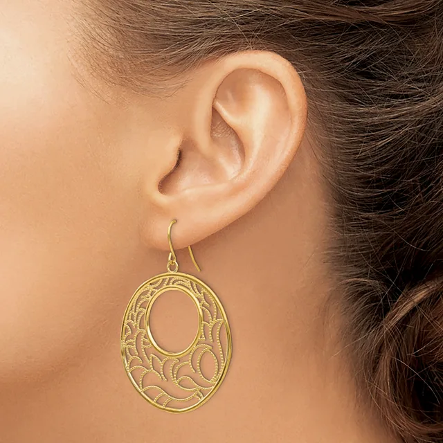 A woman wearing a gold-toned oval filigree dangle earring with an open cutout design featuring organic curved patterns.