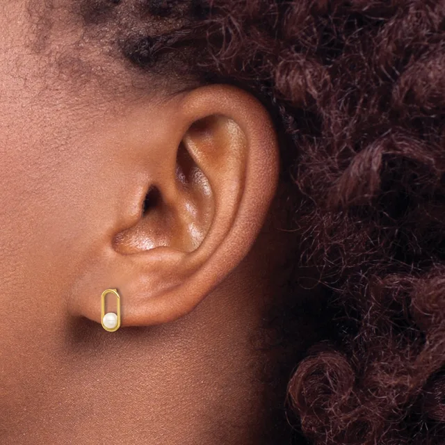 A person wearing a small gold oval hoop earring in their earlobe, shown in profile against dark curly hair.