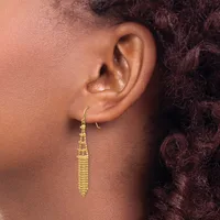 A person wearing a long tapered gold-toned beaded dangle earring hanging from a hook fastening, shown from the side profile of their ear and neck.