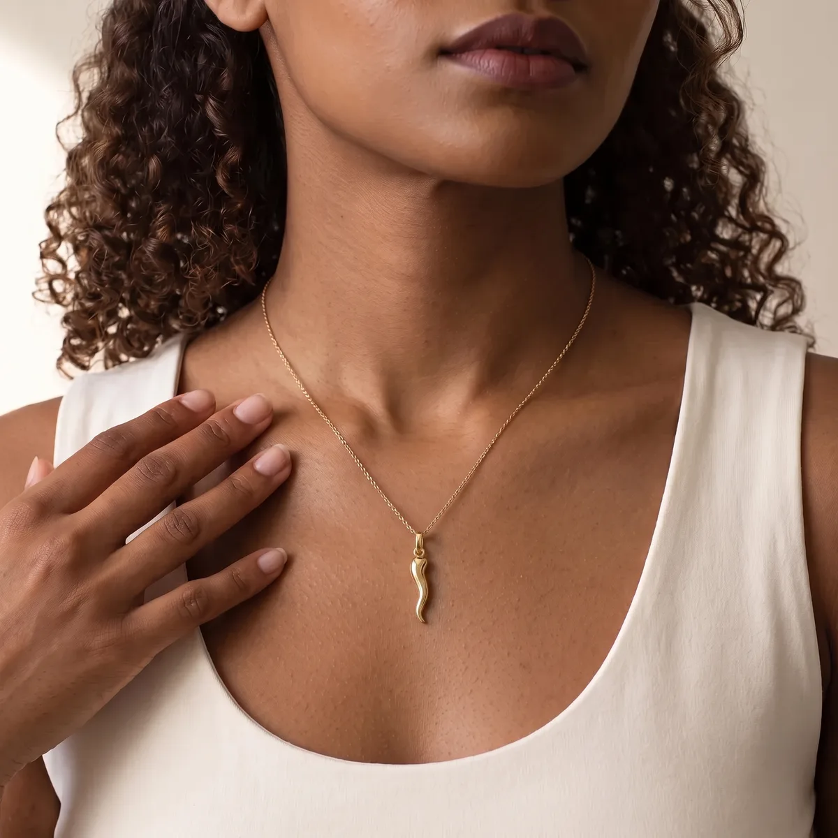 A woman wearing a white sleeveless top displays a delicate gold chain necklace with a curved horn-shaped pendant.
