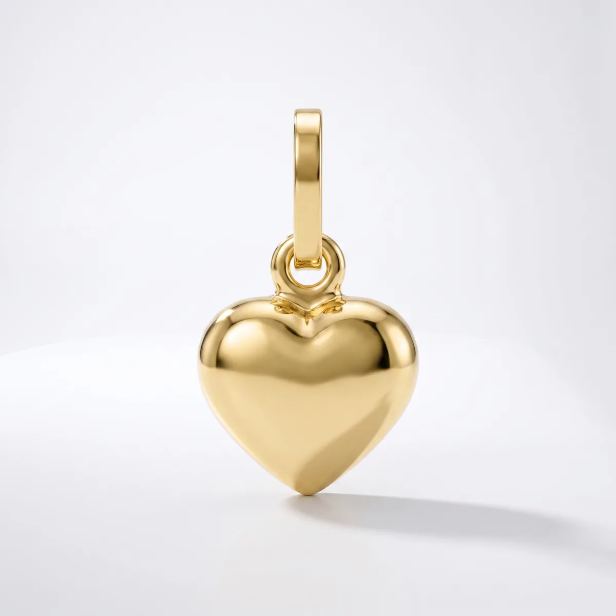 A polished gold heart-shaped pendant with a rectangular bail loop attached to the top, displayed against a white background.