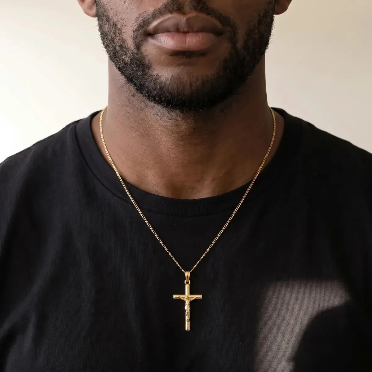 A man wearing a black t-shirt and gold chain necklace with a gold cross pendant.