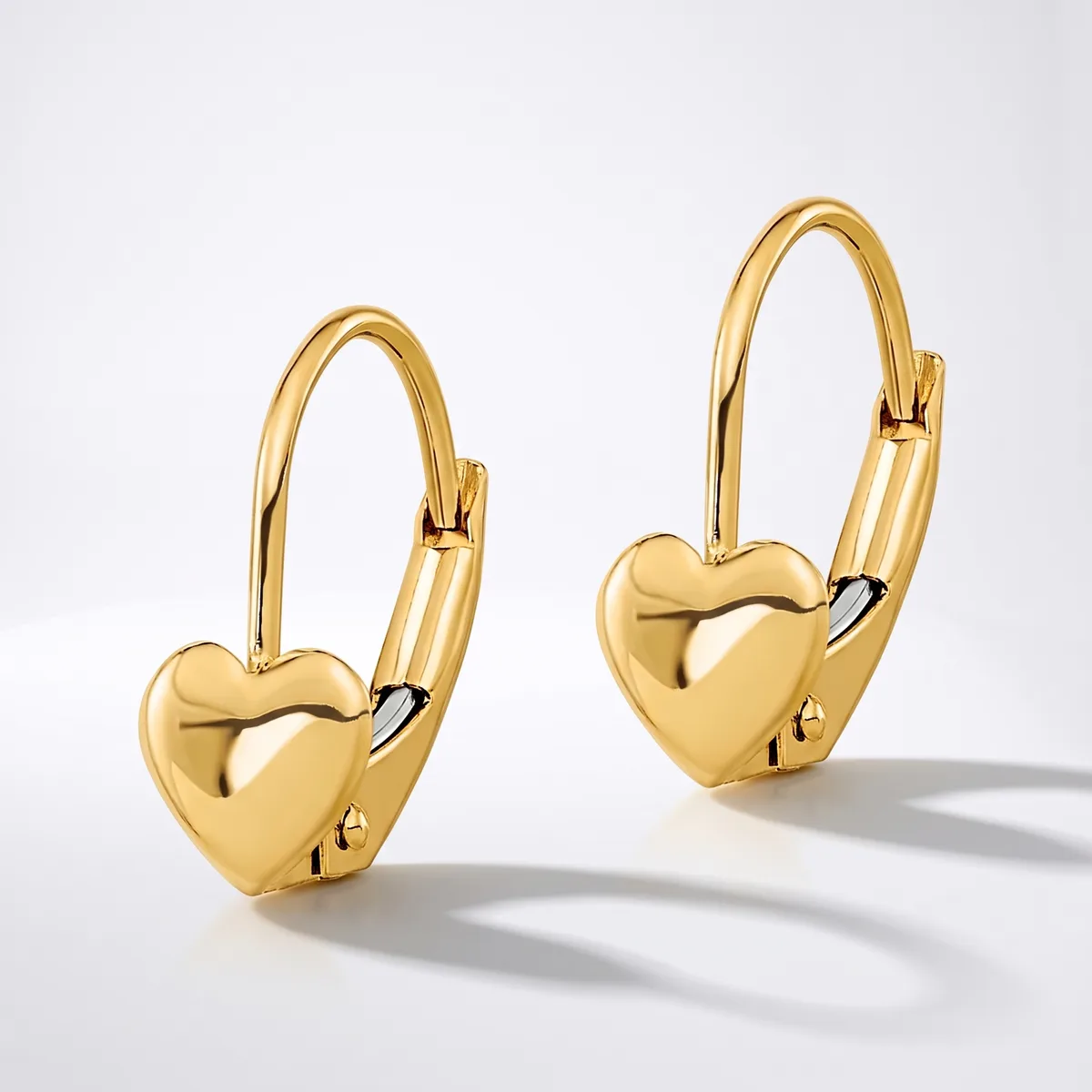 A pair of glossy gold heart-shaped leverback earrings with a hinged hook and a small stamped hallmark on the back of each heart, displayed against a white background.