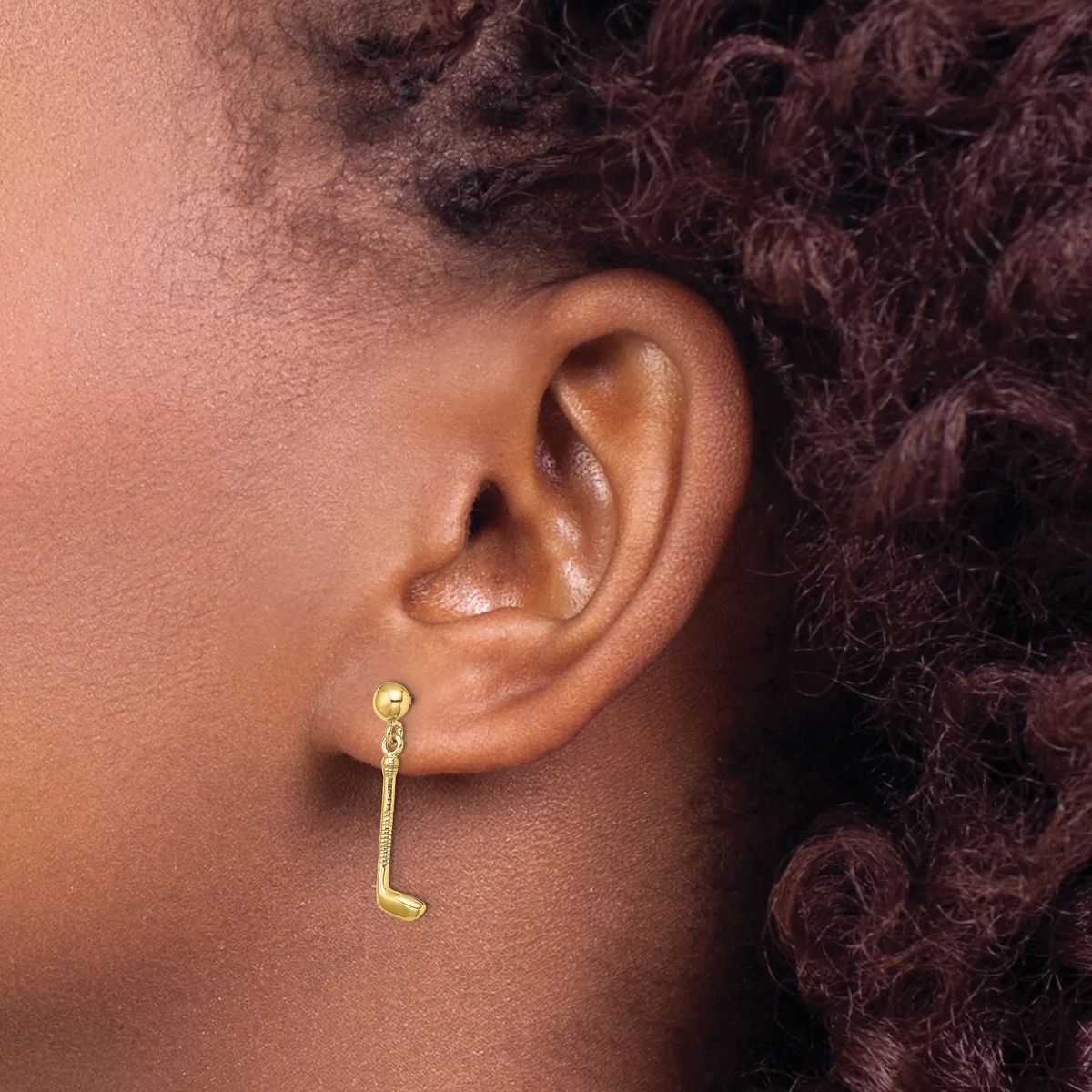 A gold hook-style earring hangs from the earlobe of a person with dark curly hair and brown skin.