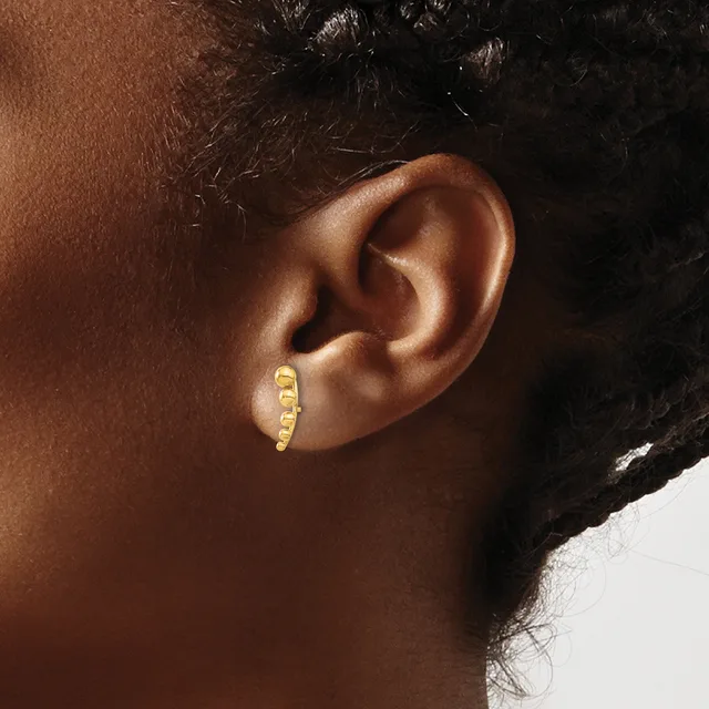 A close-up view of a person's ear wearing a small gold curved earring with a textured surface.