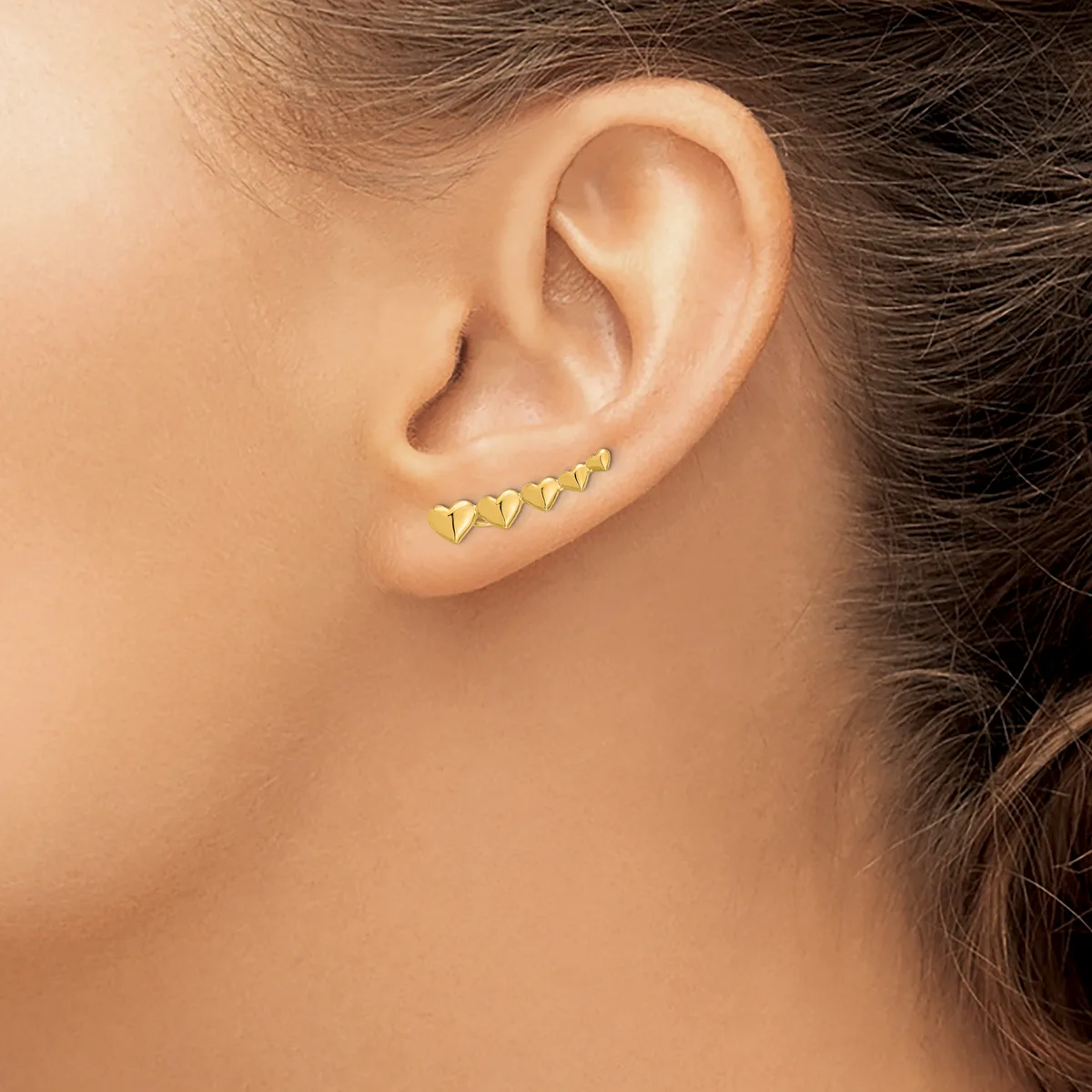 A person wearing a row of small gold triangular stud earrings along the lower portion of their earlobe.