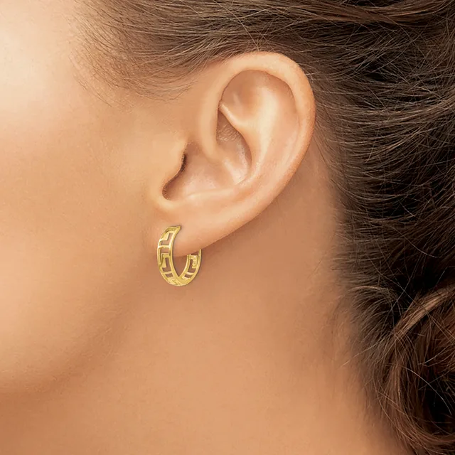 A person wearing small gold hoop earrings with a geometric Greek key pattern, shown from the side profile against their ear.