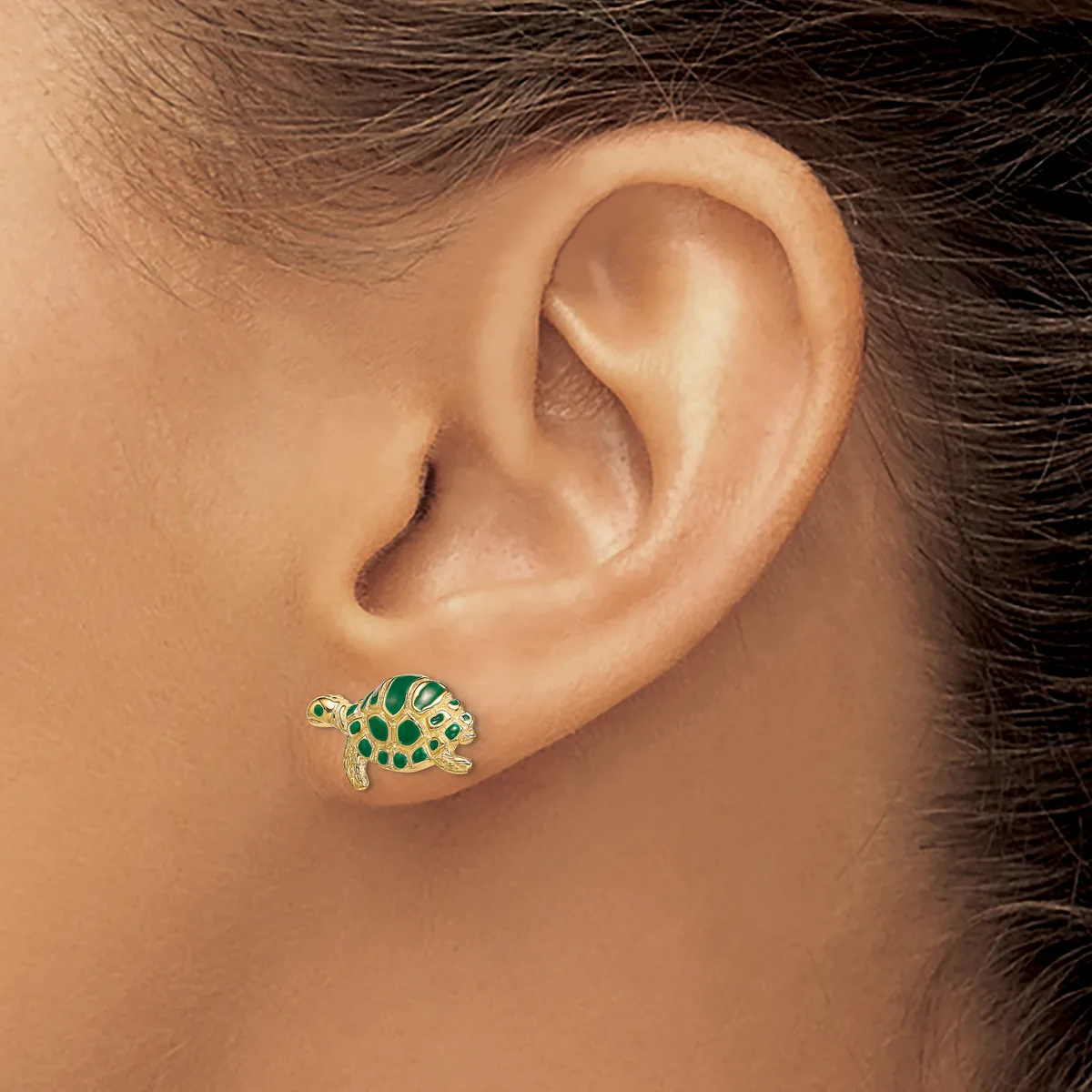 A gold fish-shaped earring with green enamel and yellow spots worn on a person's earlobe.
