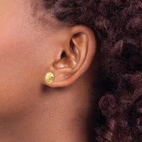 A close-up side view of a person's ear wearing a small oval gold stud earring with a textured surface.