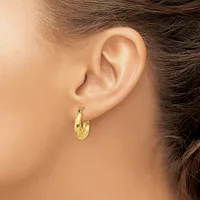 A woman wearing a pair of polished gold hoop earrings with a textured finish, shown from the side profile of her ear and neck.