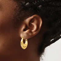 A person wearing a pair of gold-colored hoop earrings with a textured, hammered surface finish on their earlobe.