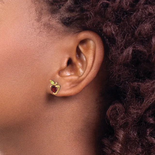 A person wearing a small gold heart-shaped stud earring with a red gemstone in the center, shown from the side profile.