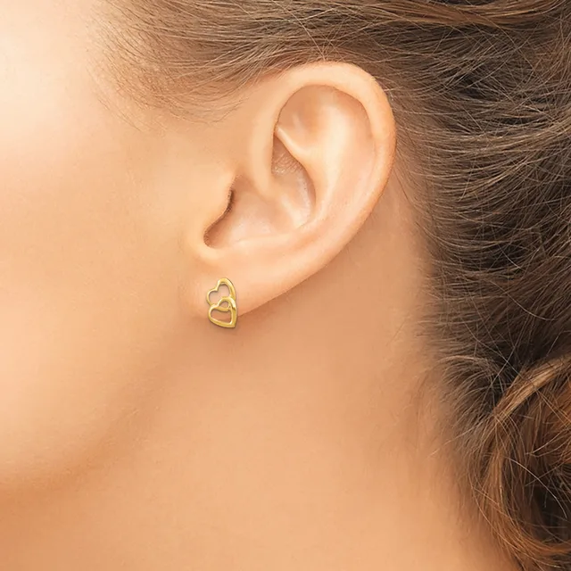 A woman wearing a gold interlocking heart stud earring in her earlobe, shown from the side profile.