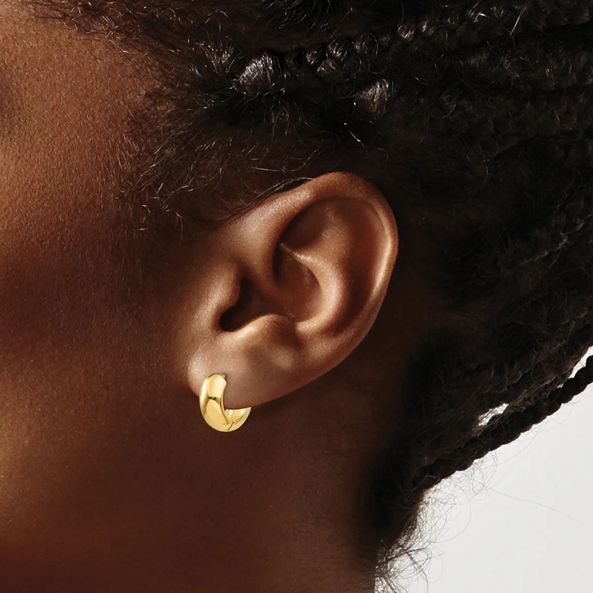 A person wearing a gold crescent-shaped hoop earring in their earlobe, shown in profile against a neutral background.