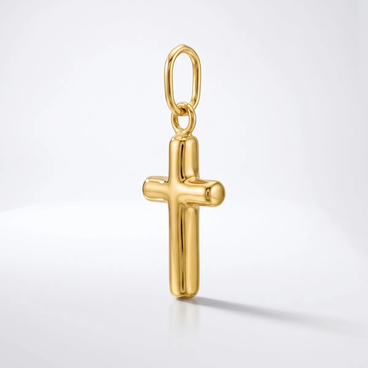 A polished gold cross pendant with rounded edges hangs from a small oval bail loop against a white background.