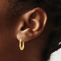 A person wearing a pair of gold hoop earrings with a textured finish, shown from the side profile of their ear.