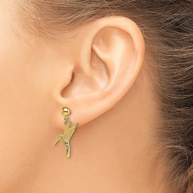 A gold-toned parrot charm earring hanging from a ball post on a person's earlobe.