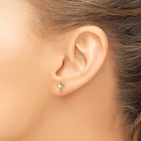 A person wearing a small cross-shaped earring with a pale green stone in the center, shown from the side view against their ear.