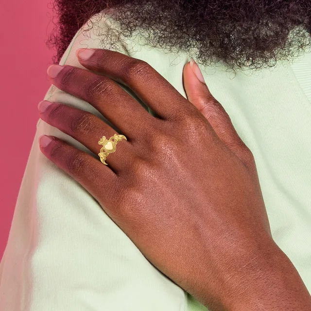 A dark-skinned hand resting on a shoulder, wearing a gold Claddagh ring with a heart, crown, and two hands design on the ring finger.