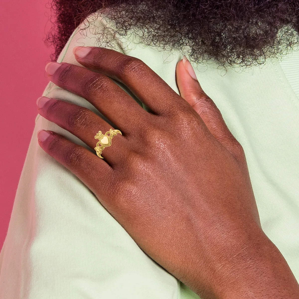 A dark-skinned hand resting on a shoulder, wearing a gold Claddagh ring with a heart, crown, and two hands design on the ring finger.