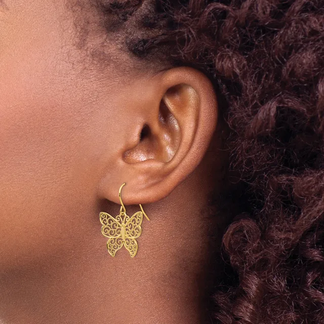 A person wearing gold filigree butterfly earrings with curved hooks, shown in profile view against dark curly hair.