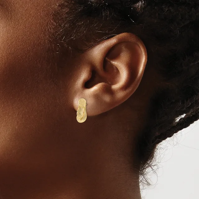 A person wearing a small gold hoop earring with a textured surface is shown in profile from the side of their face and ear.