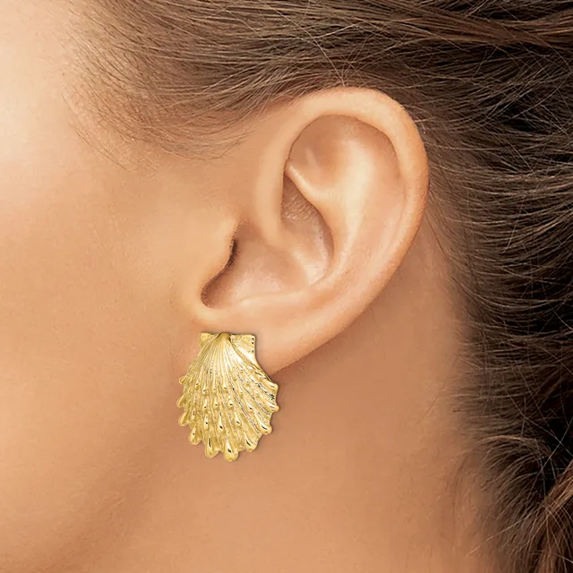 A gold shell-shaped stud earring worn on a person's earlobe, shown from the side view against their neck and shoulder.