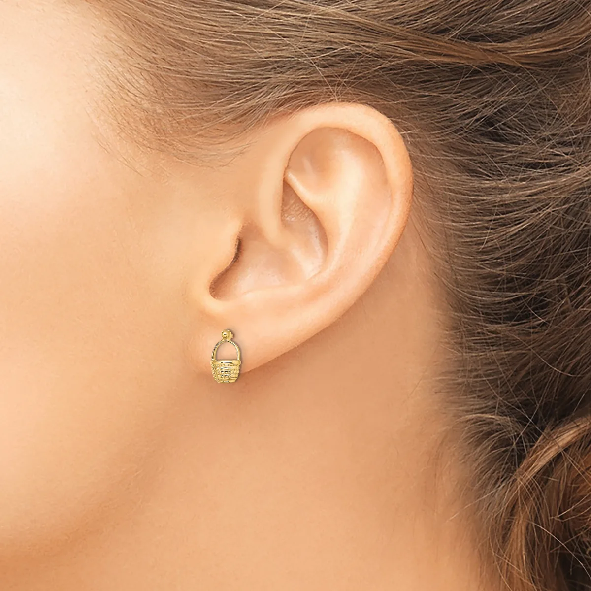 A person wearing a small gold oval earring with a textured surface, shown from the side profile view of their ear.