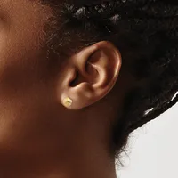 A gold stud earring worn in the earlobe of a person shown in profile, with dark curly hair pulled back.