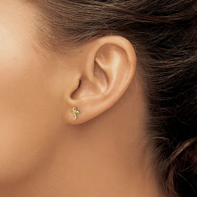 A small cross-shaped earring with gemstone accents in the earlobe of a person with dark hair and medium skin tone.
