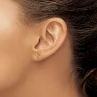 A small cross-shaped earring with gemstone accents in the earlobe of a person with dark hair and medium skin tone.